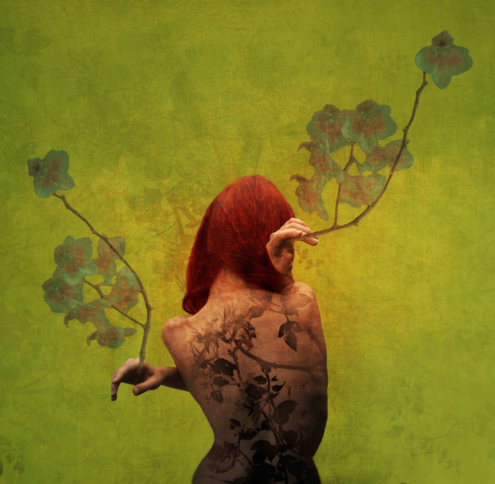 A woman showing her back, featuring a detailed tattoo design and flowers bloosoming from her hands